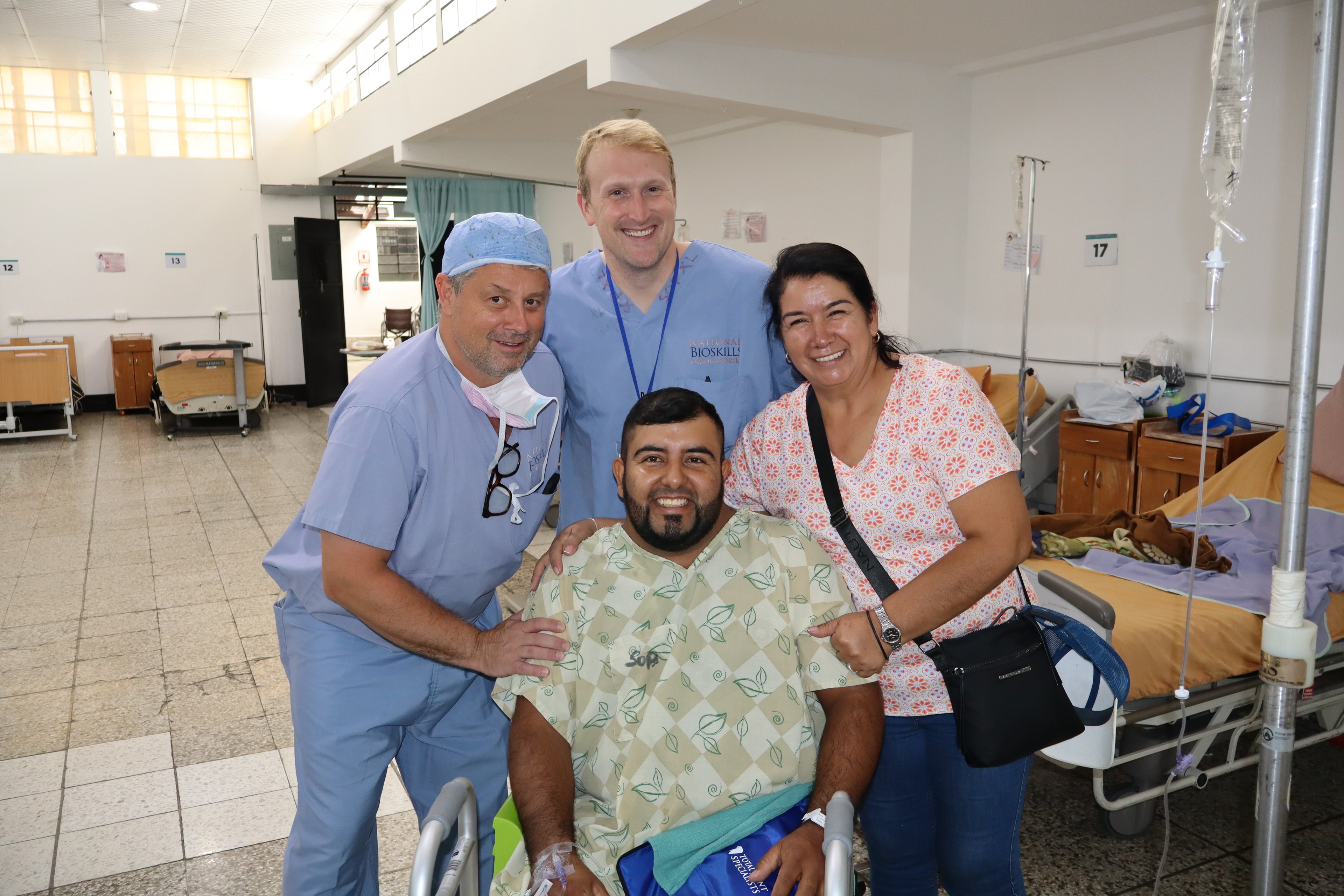 A patient sits with three people beside a walker in the ward.